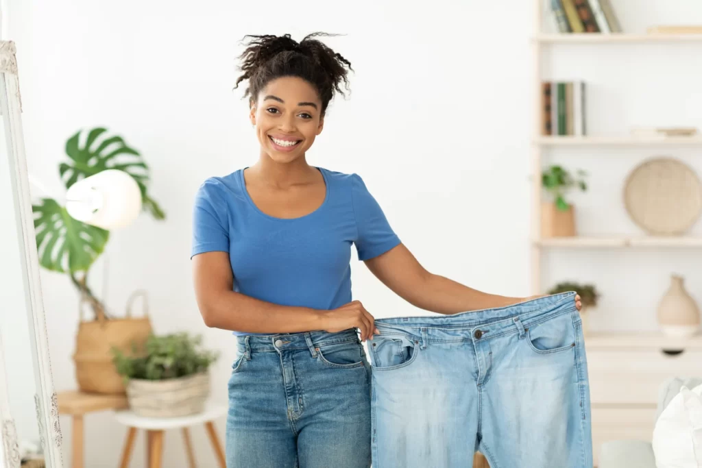 happy woman holding oversized jeans in bright home utc